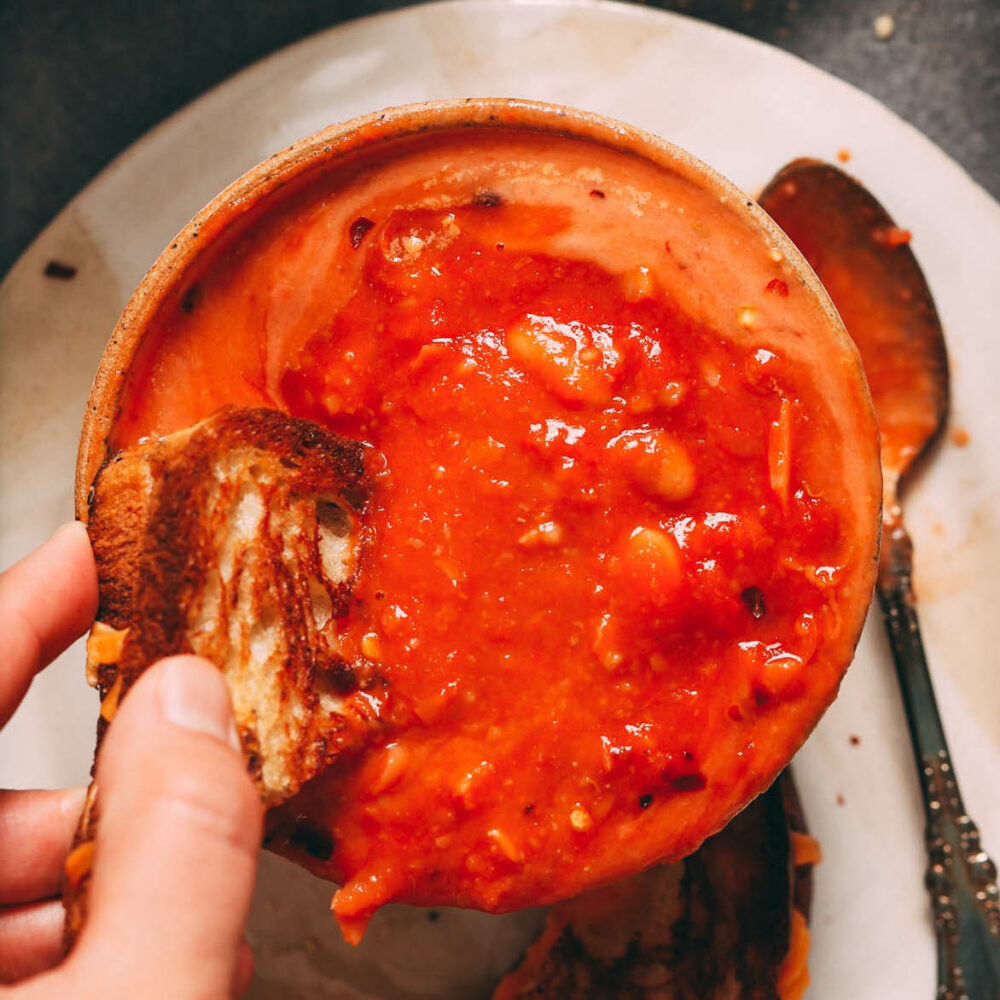 Mencelup sandwic keju panggang ke dalam mangkuk sup tomato