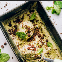 Cuillère à crème glacée dans un récipient de crème glacée aux pépites de chocolat à la menthe végétalienne sans baratte avec des feuilles de menthe et des pépites de chocolat sur le dessus