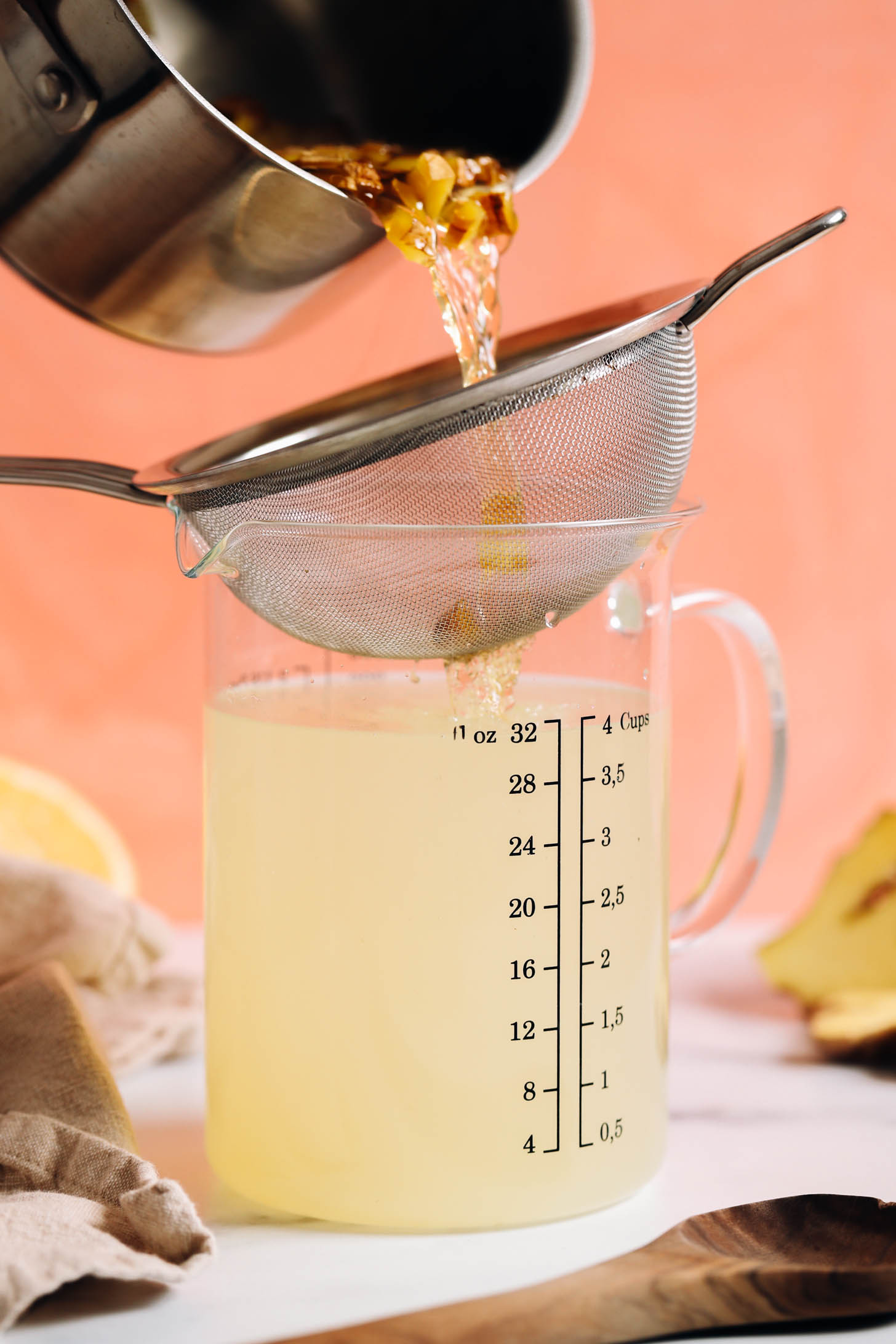 Straining a ginger agave mixture into a measuring glass of lemon water