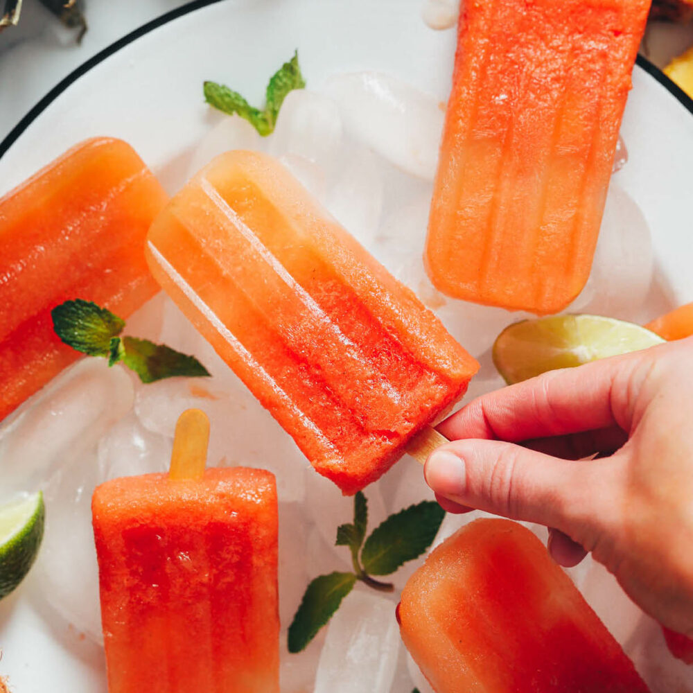 Picking up a homemade fruit popsicle from a plate of ice cubes