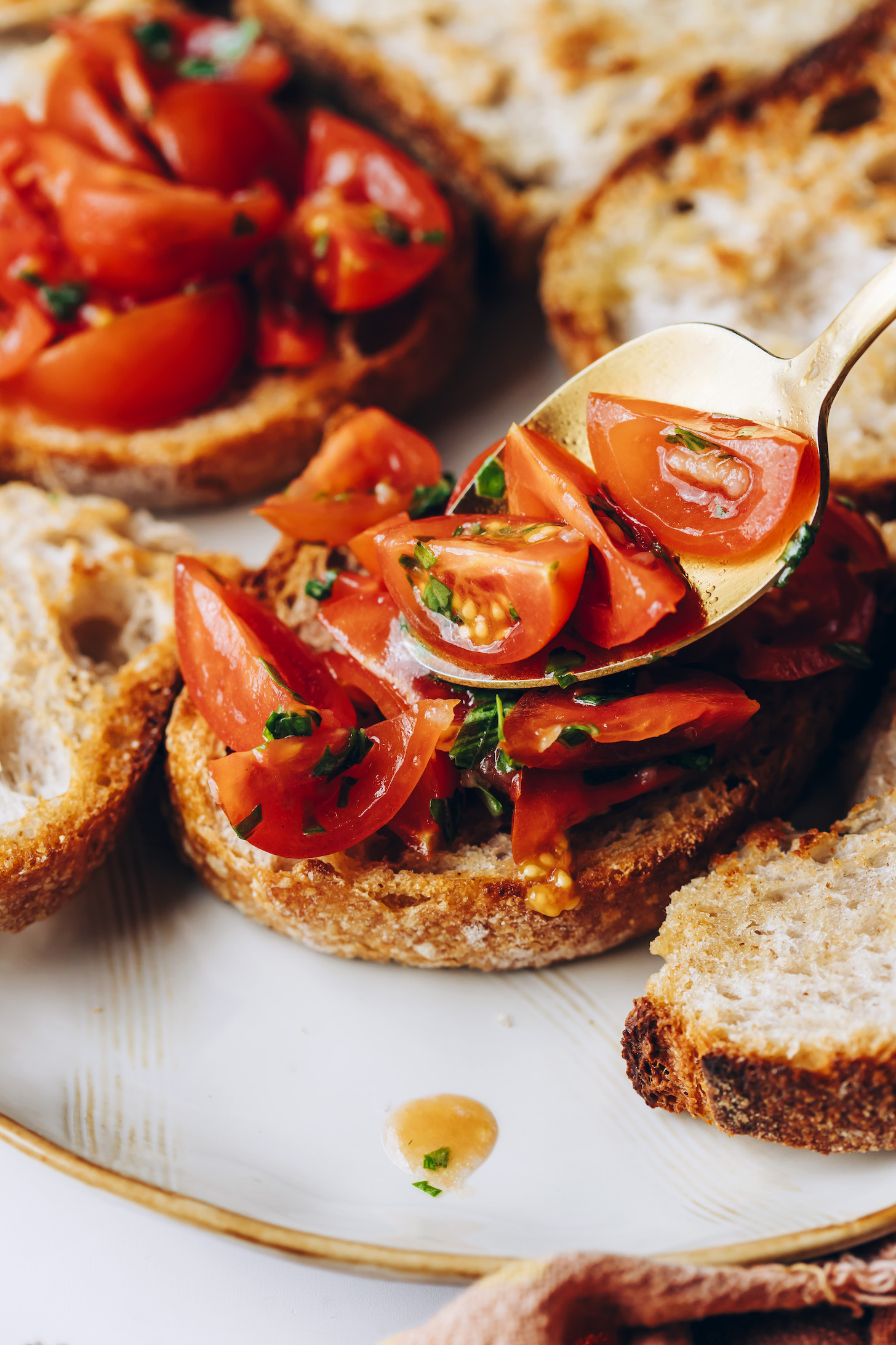 Bir kaşık kullanarak kiraz domates ve fesleğen karışımını kızarmış ekmek üzerine aktarmak