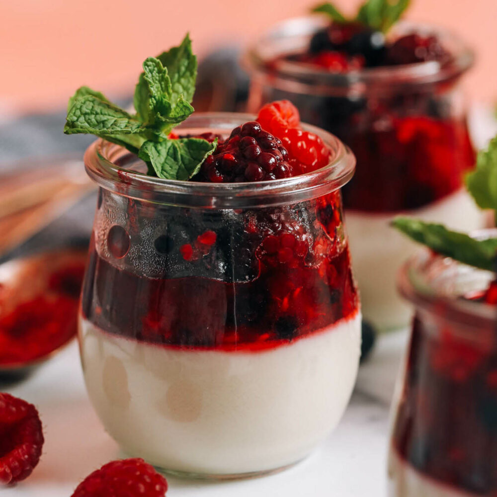 Close up shot of a jar of vegan vanilla panna cotta with a mixed berry compote