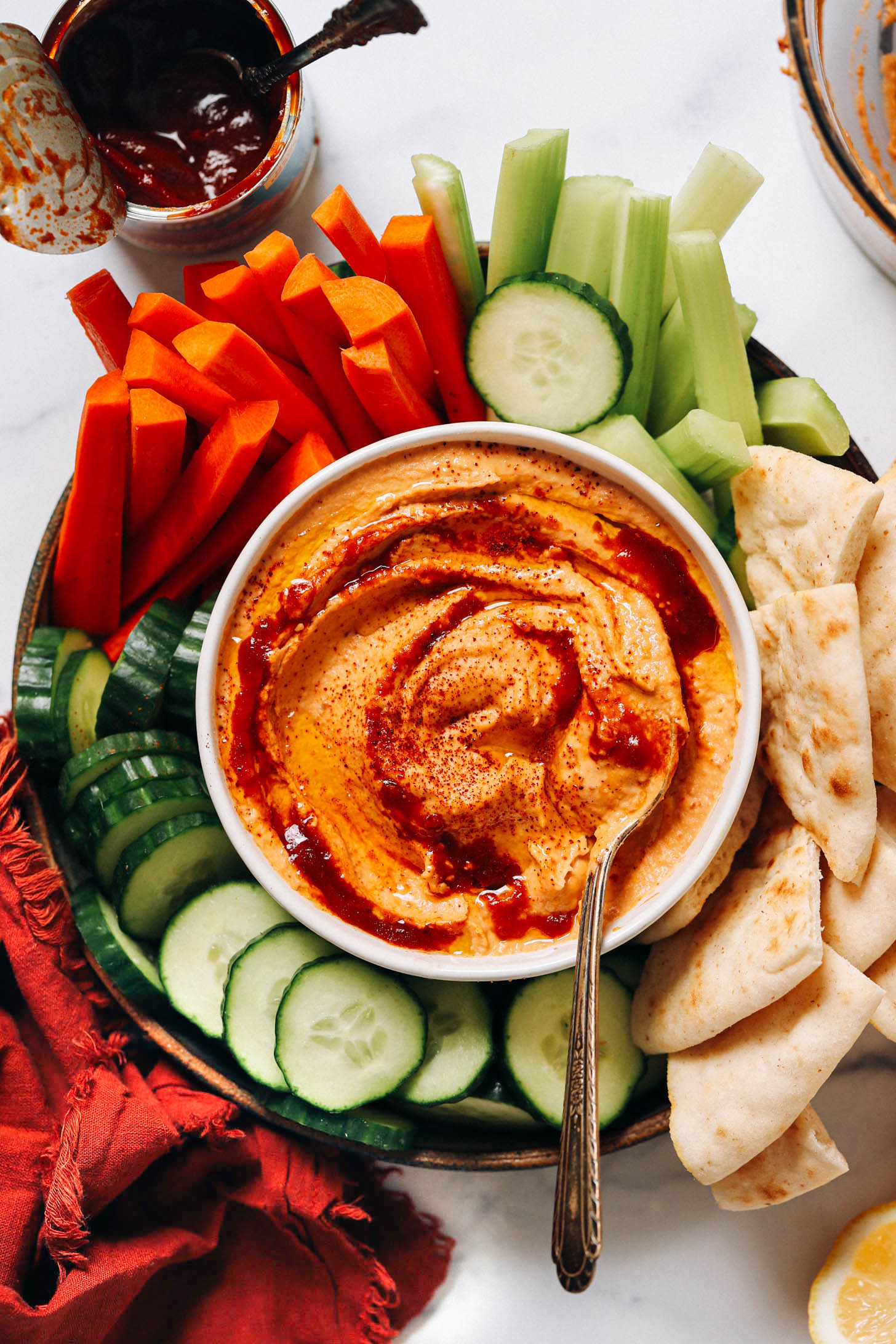 Bowl of spicy chipotle hummus surrounded by veggies and pita bread