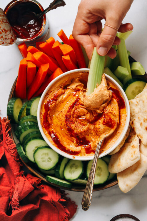 Dipping a celery stick into a bowl of our spicy chipotle hummus recipe
