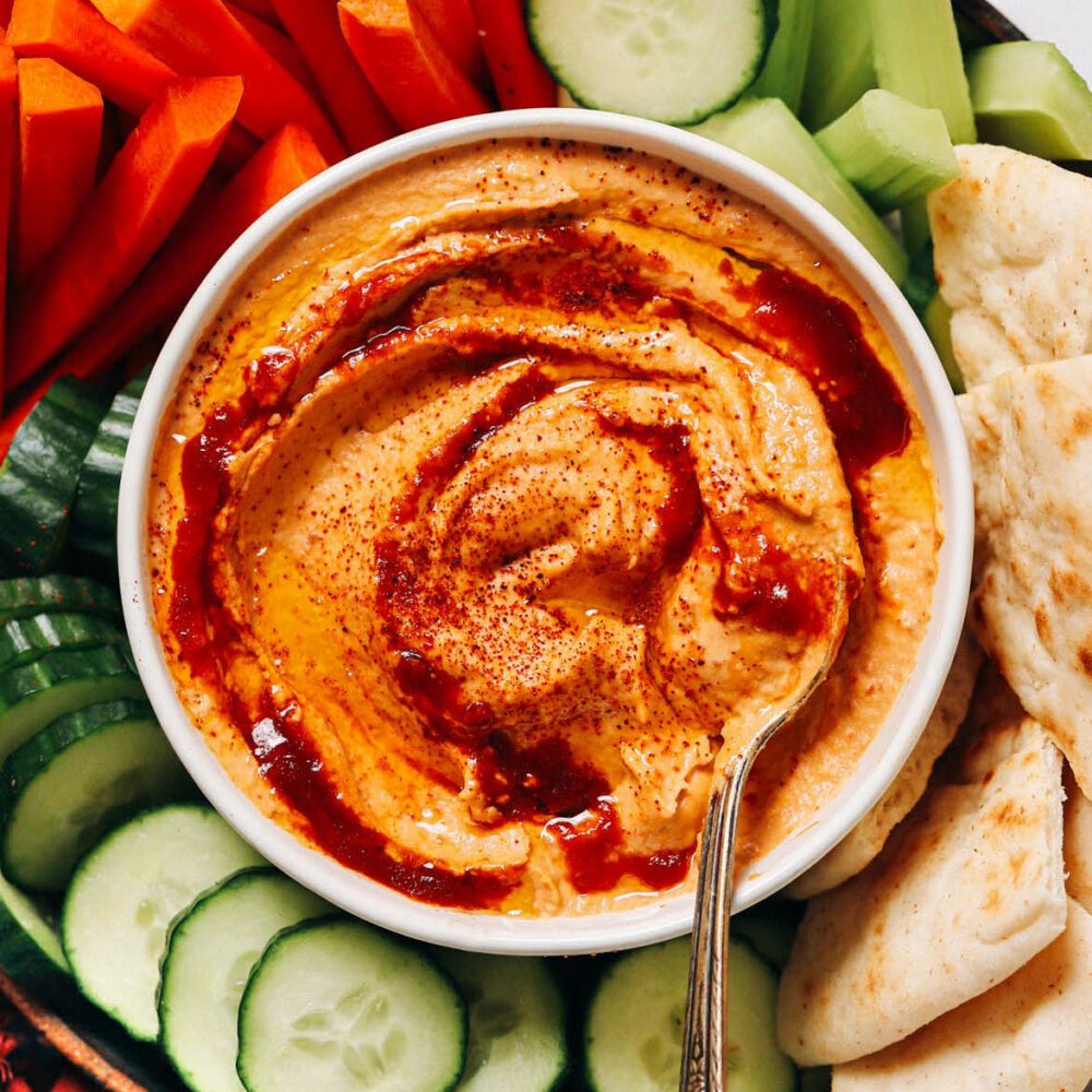 Overhead shot of a bowl of spicy chipotle hummus surrounded by pita and veggies for dipping