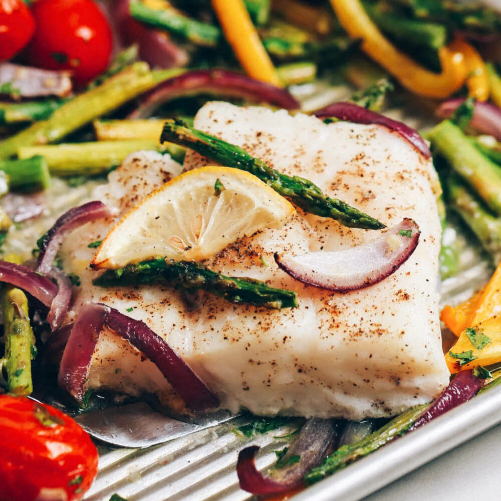 Close up shot of baked cod and spring vegetables on a baking sheet