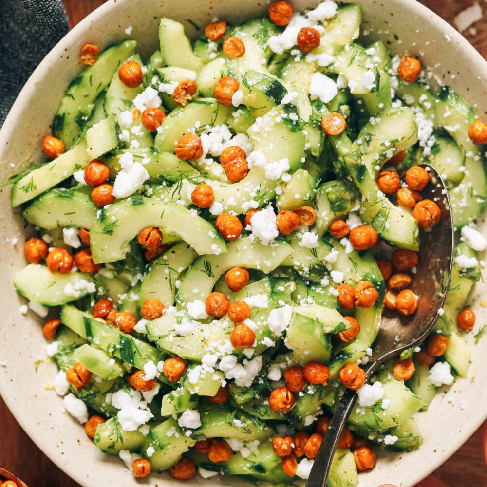 Bowl of cucumber salad with fresh dill and mint and topped with crispy chickpeas and vegan feta