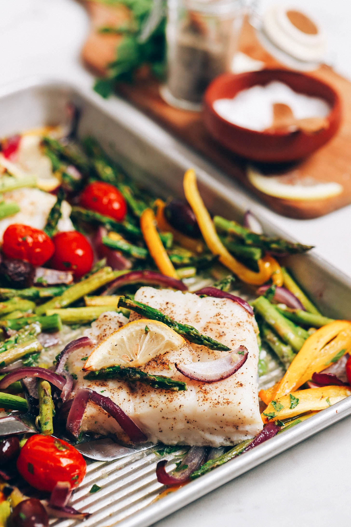 Baked cod fillet on a sheet pan with lemon slices and vegetables
