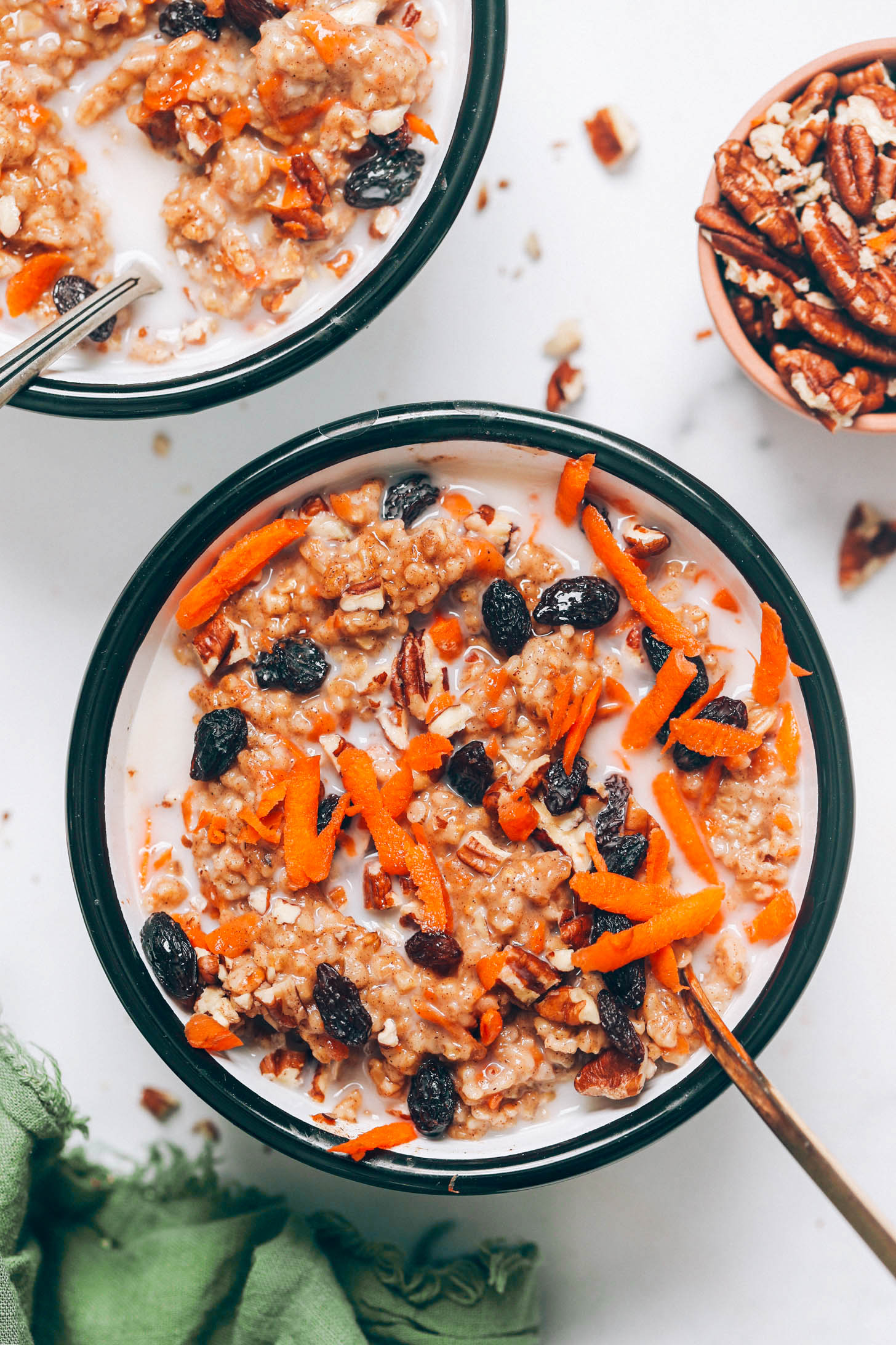 Two bowls of carrot cake oatmeal topped with raisins and grated carrots