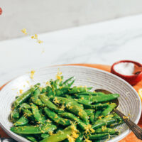 Zesting a lemon over a bowl of perfectly cooked sugar snap peas
