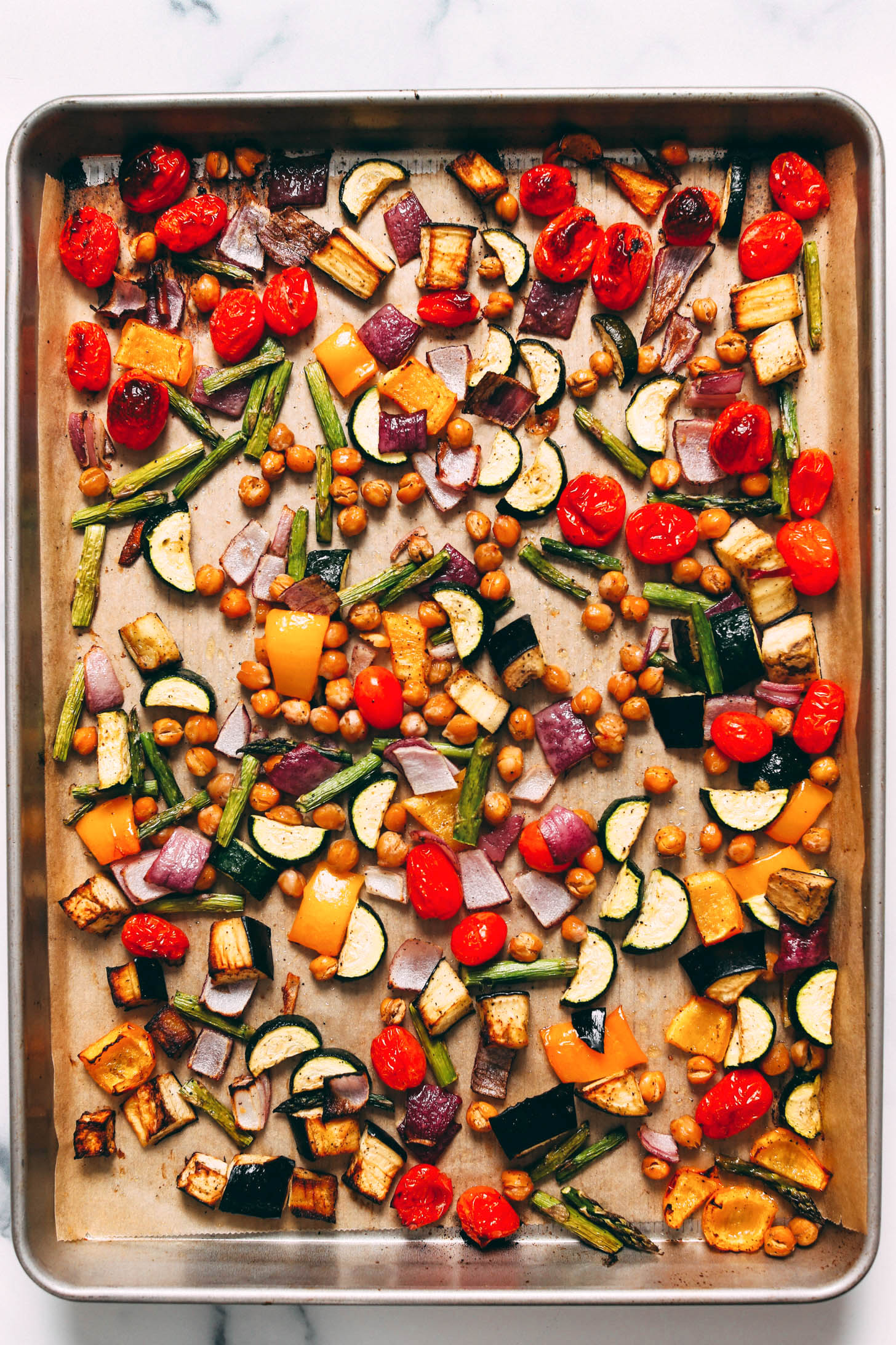 Baking sheet with roasted eggplant, cherry tomatoes, zucchini, asparagus, chickpeas, and bell peppers