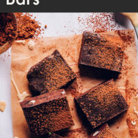 Spread of vegan and gluten-free fudgy tahini date chocolate bars with cocoa powder sprinkled on top