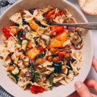 Hand holding a bowl of vegan pasta primavera