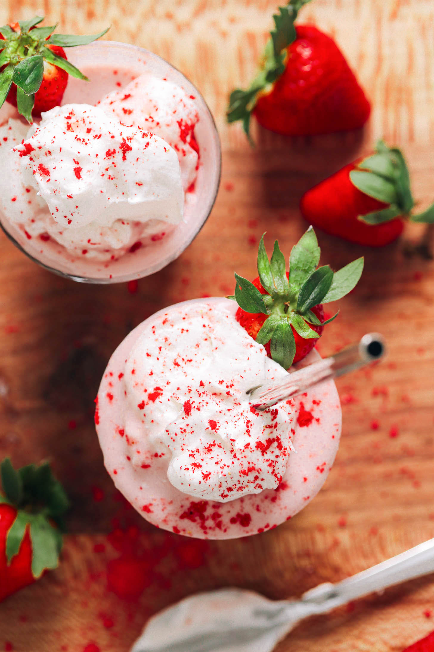 Photo aérienne de deux milkshakes aux fraises végétaliens garnis de crème fouettée à la noix de coco et de fraises lyophilisées