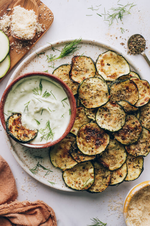 Plate of baked zucchini slices next to a bowl of vegan ranch