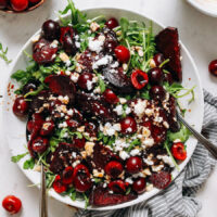 Overhead shot of a roasted beet and arugula salad with fresh cherries and candied hazelnuts