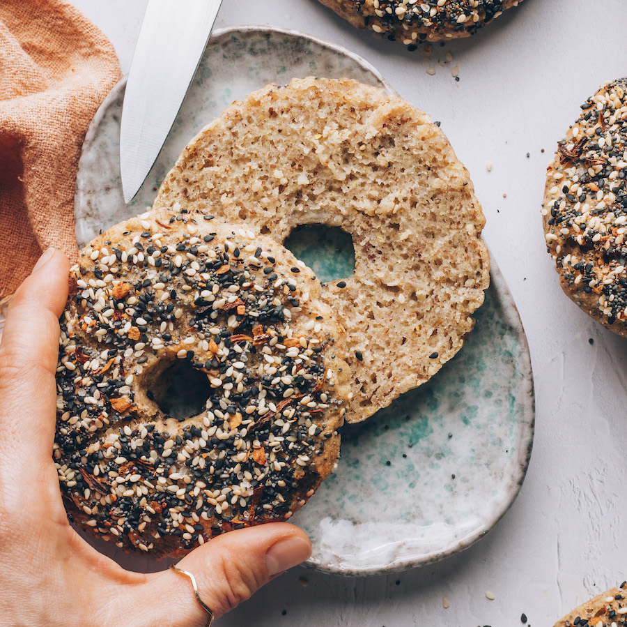 Hand lifting half of a gluten-free everything bagel to show the inner texture
