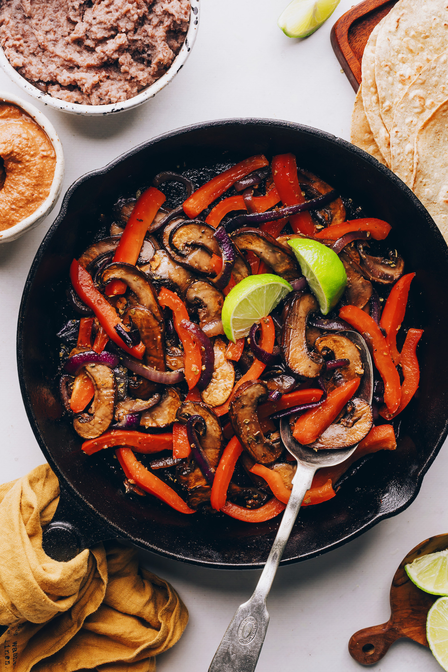 Lime wedges on sautéed peppers, onions, and mushrooms in a cast iron skillet