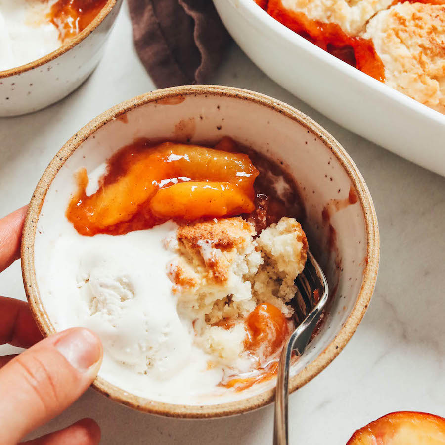 Fork in a bowl of gluten-free peach cobbler with vegan vanilla ice cream