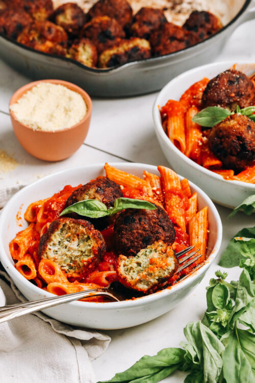 Skillet of turkey meatballs behind two bowls of pasta with meatballs