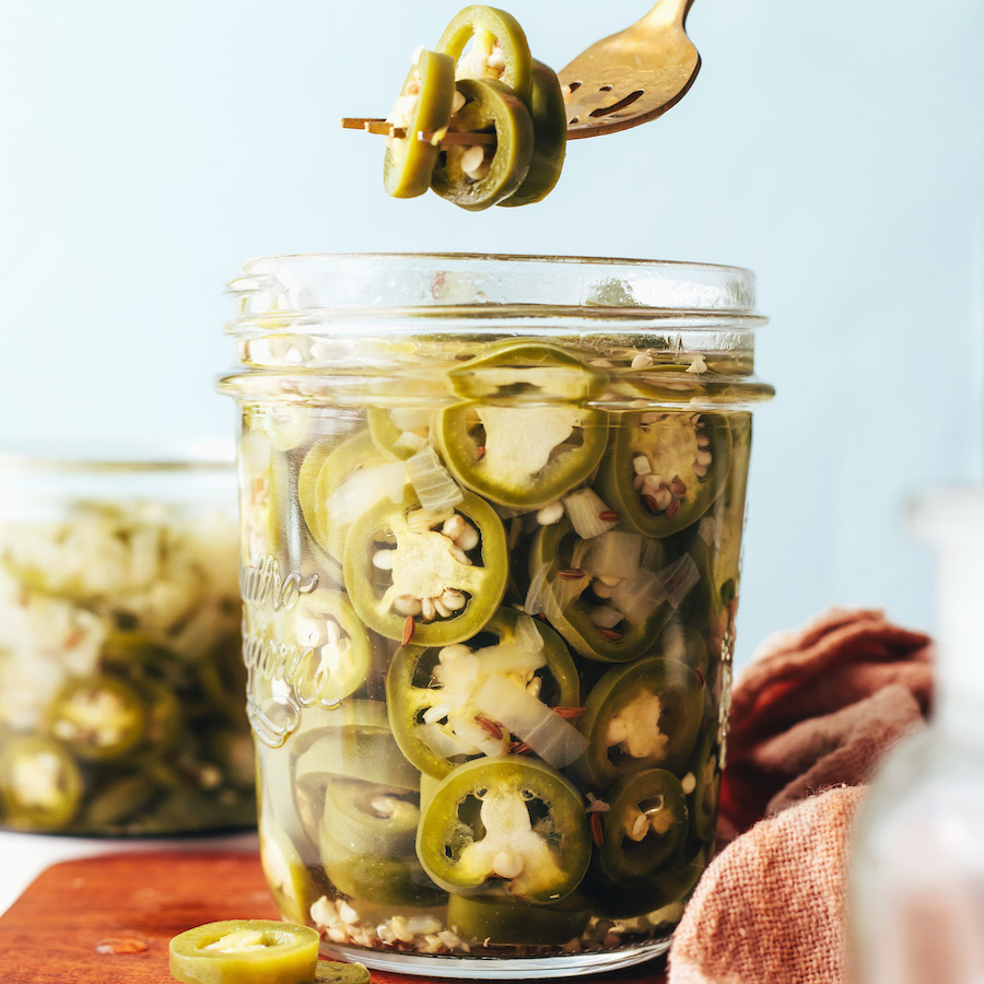 Pickled jalapenos on a fork over a jar of more of them
