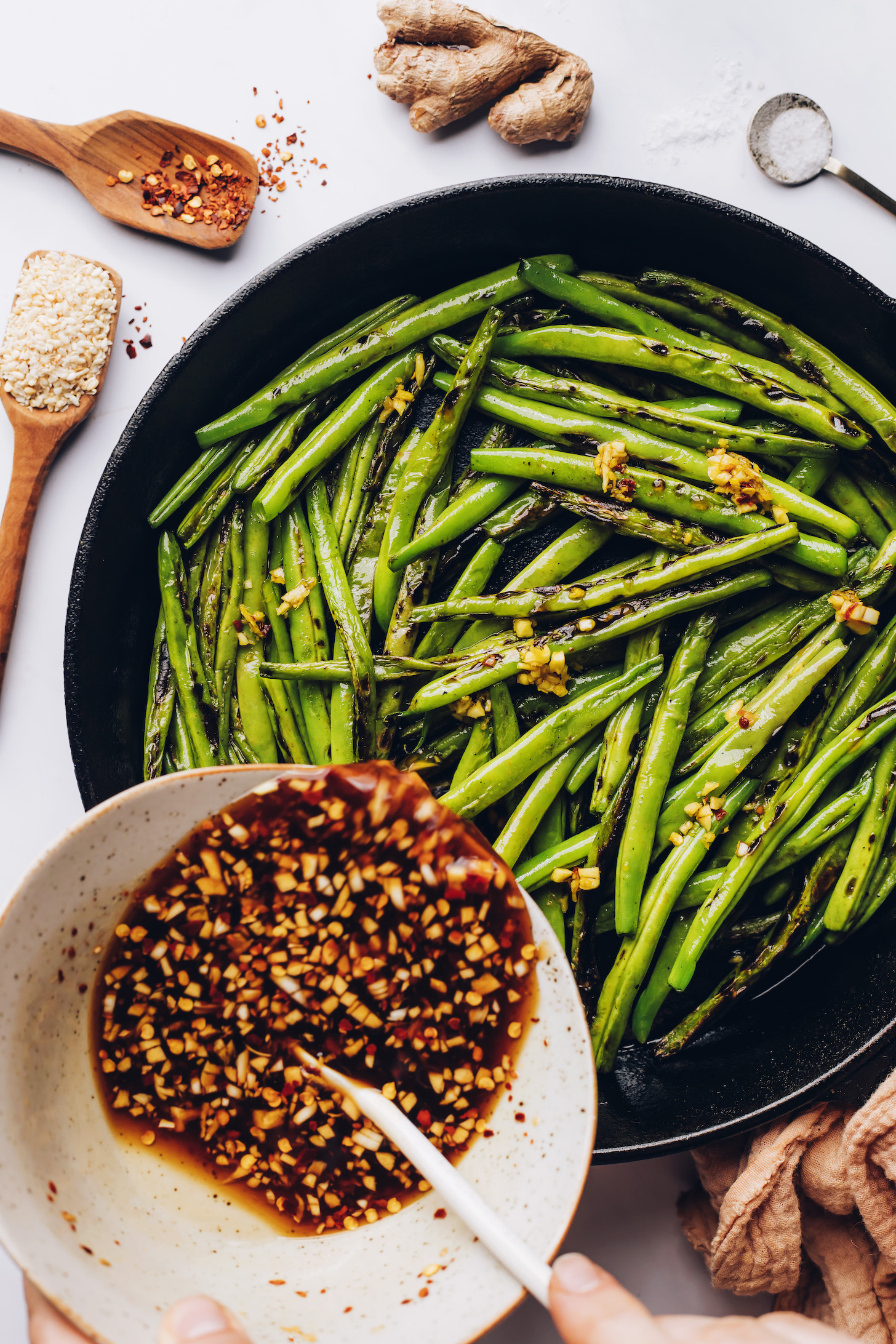 Pouring a savory Asian-inspired sauce into a skillet of blistered green beans