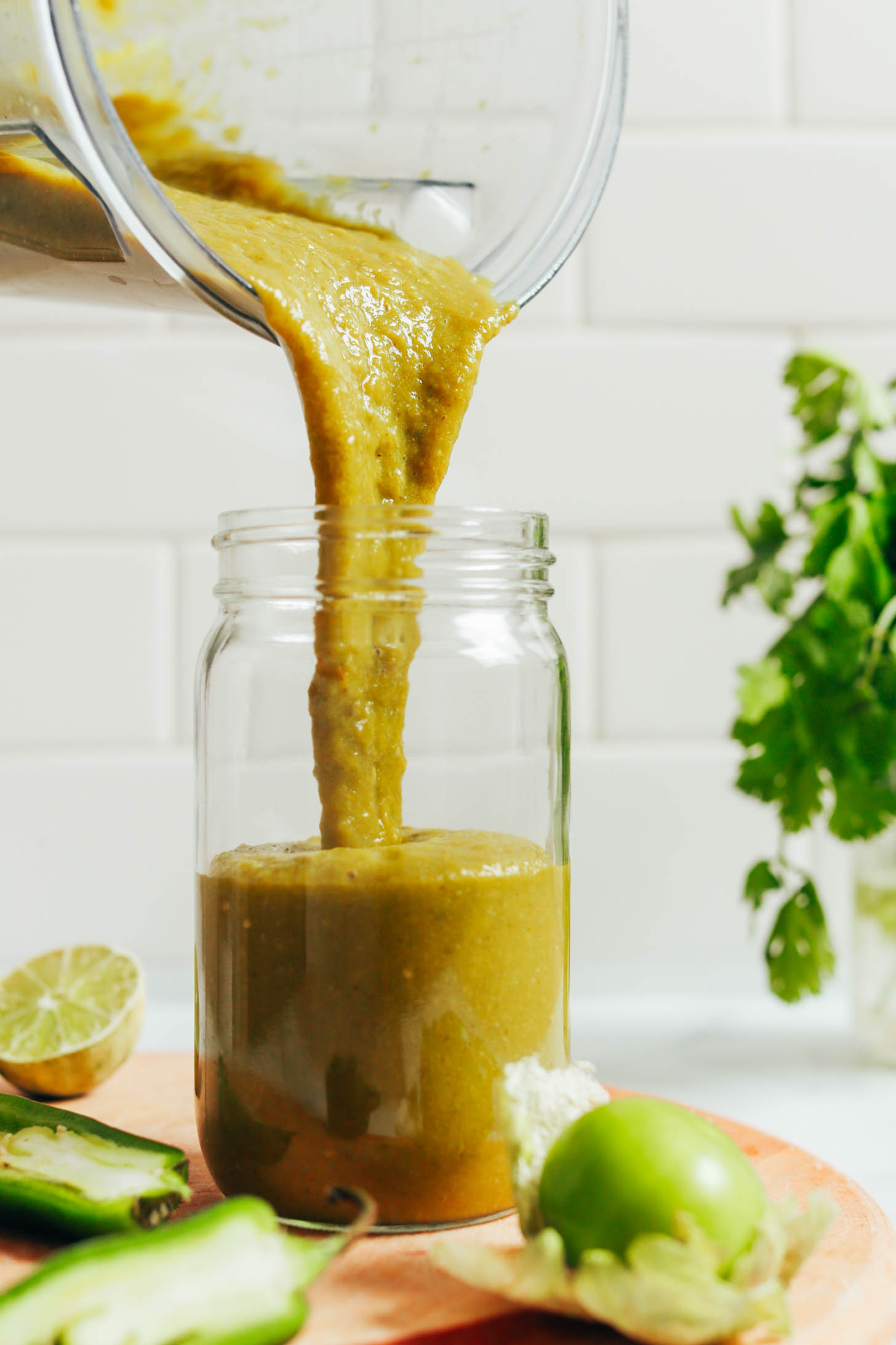 Pouring green enchilada sauce from a blender into a glass jar