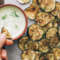 Dipping a baked zucchini slice into a bowl of vegan ranch