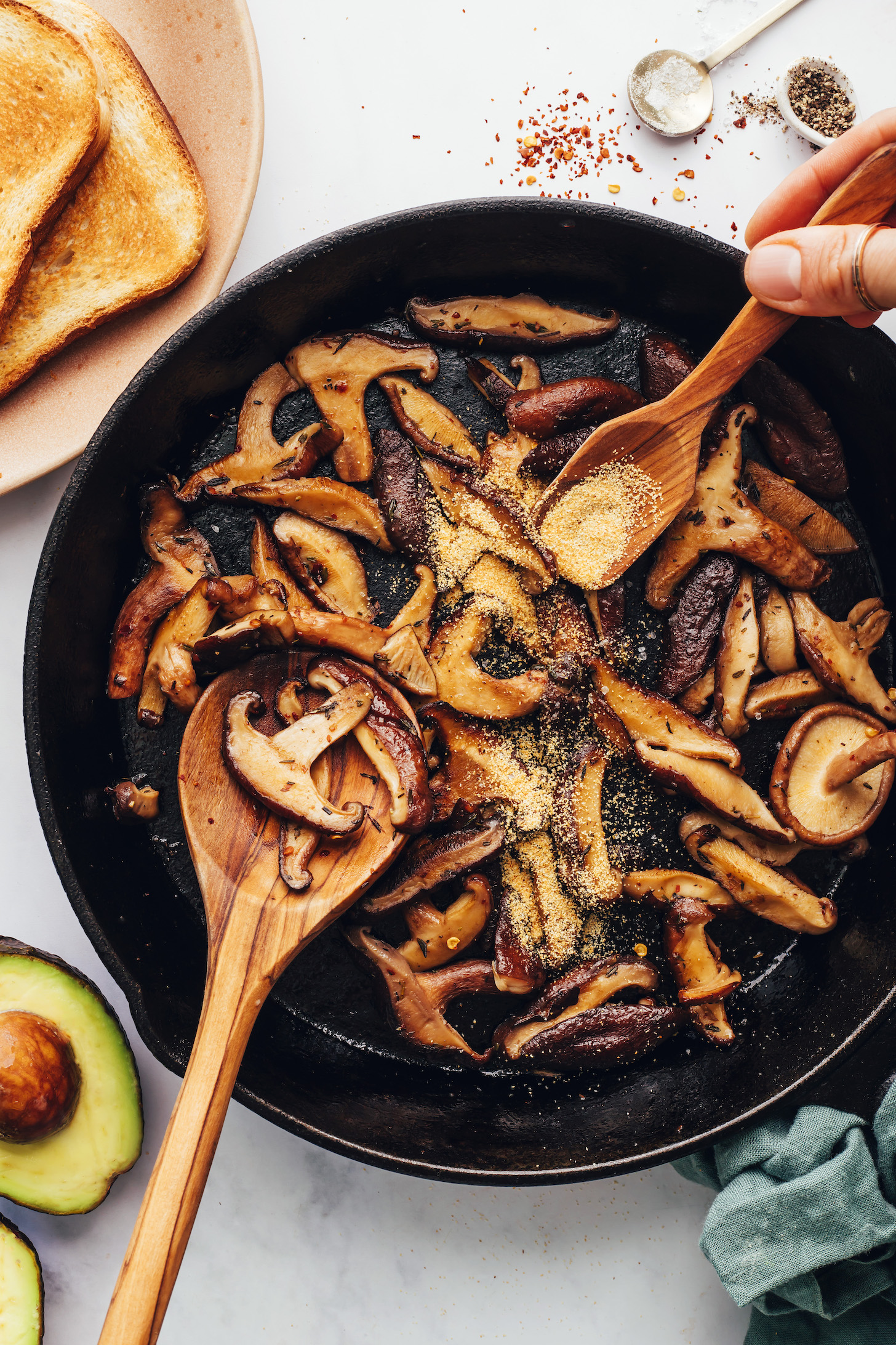 Using a small wooden spoon to sprinkle garlic powder into a pan of sautéed mushrooms