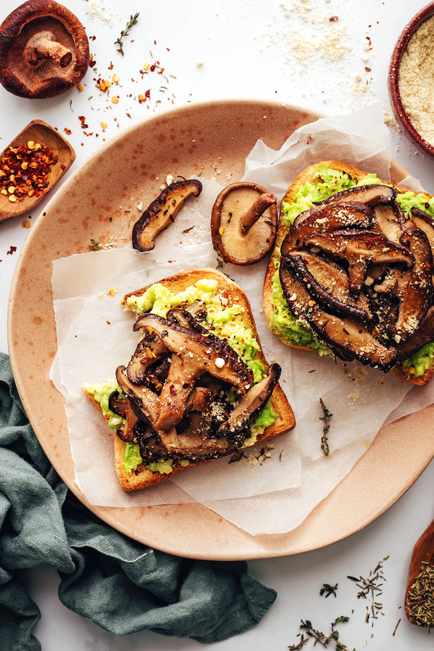 Piatto con due fette di toast di avocado ai funghi condite con scaglie di peperoncino e parmigiano vegano