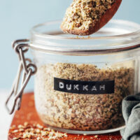 Spoonful of dukkah held above a jar of more of the spice mix