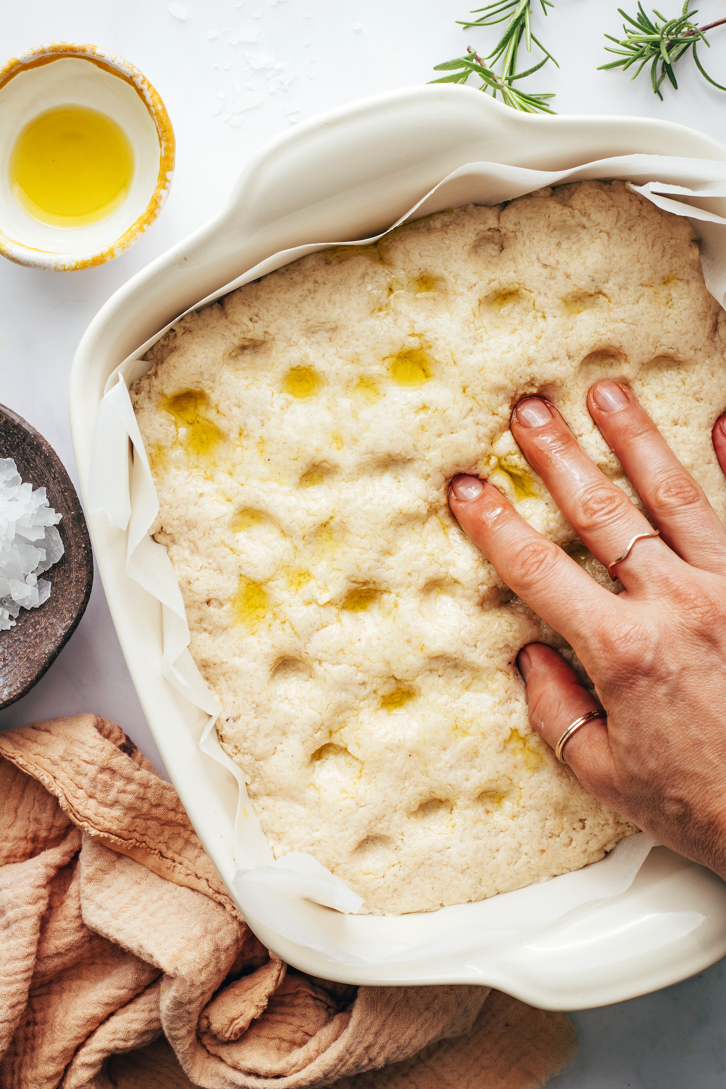 Pressing fingers into focaccia dough to create pockets on the top
