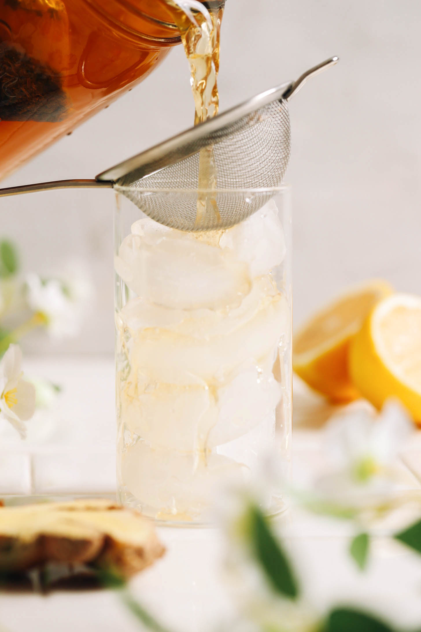 Verser le thé au jasmin et au gingembre à travers une passoire fine dans un verre de glace