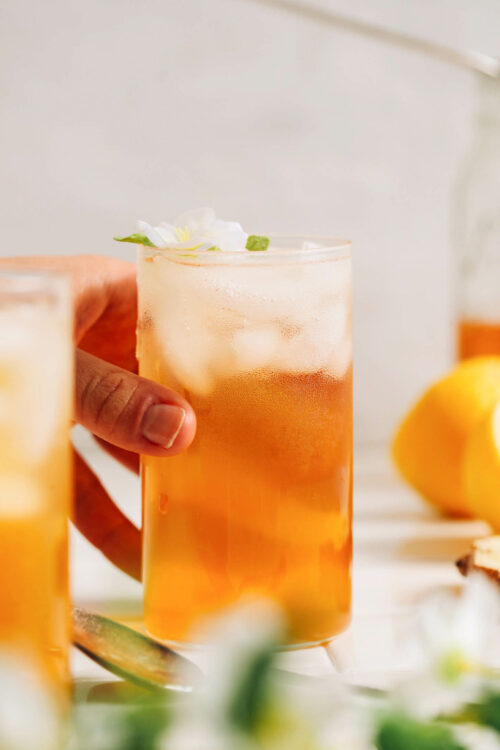 Hand reaching in to grab a glass of lemon ginger jasmine iced tea
