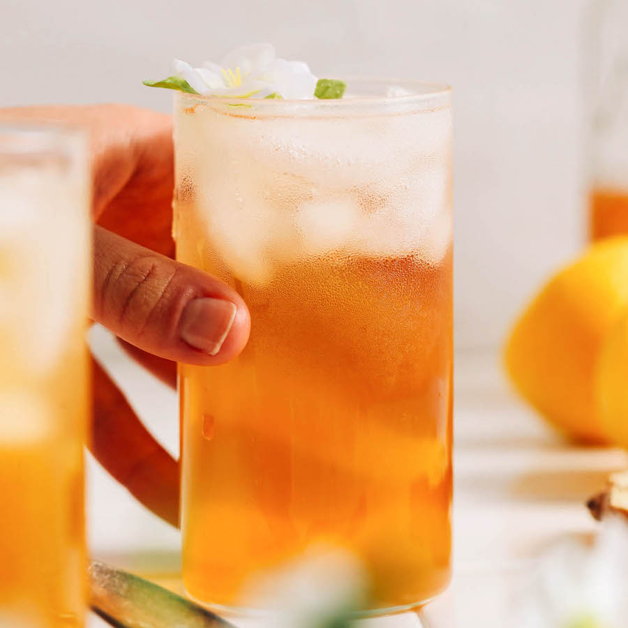Hand reaching in to grab a tall glass of lemon ginger jasmine iced tea