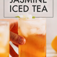 Hand reaching for a glass of jasmine ginger iced tea with text saying the recipe title above that