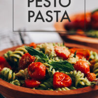 Bowl of creamy vegan pesto pasta with roasted tomatoes with text above it saying the recipe name