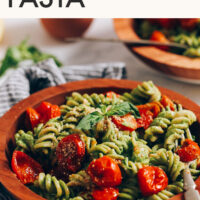 Schüssel mit cremiger veganer Pesto-Pasta mit gerösteten Tomaten, darüber Text mit dem Namen des Rezepts