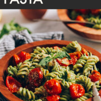 Bowl of creamy vegan pesto pasta with roasted tomatoes with text above it saying the recipe name