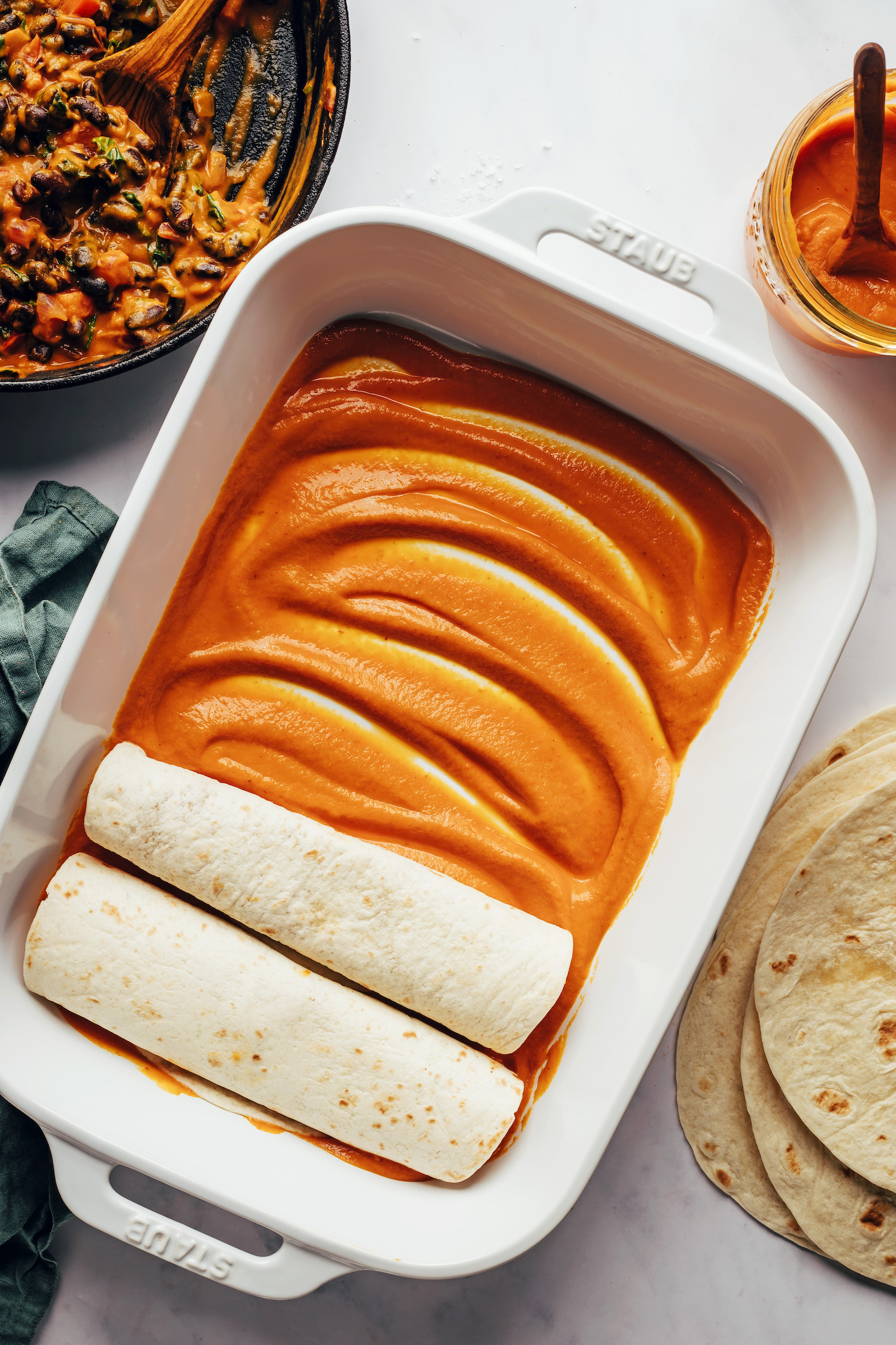 Two enchiladas in a baking dish with the bottom of the dish coated with pumpkin enchilada sauce