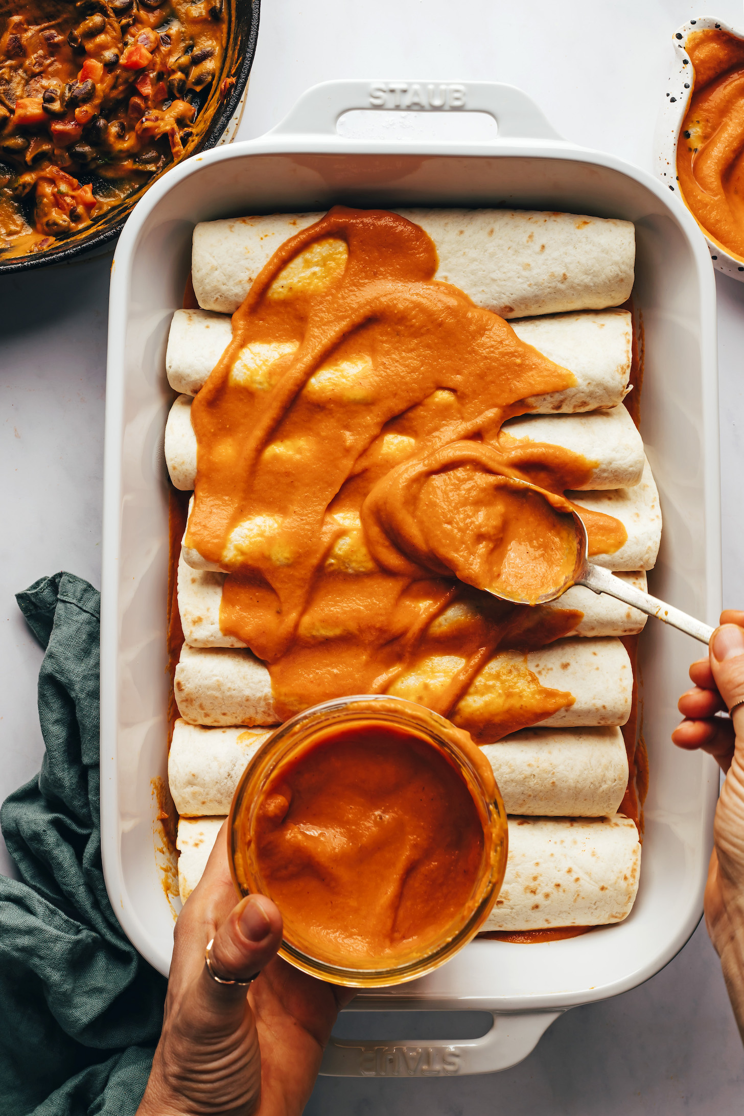 Drizzling pumpkin enchilada sauce over tortillas stuffed with filling