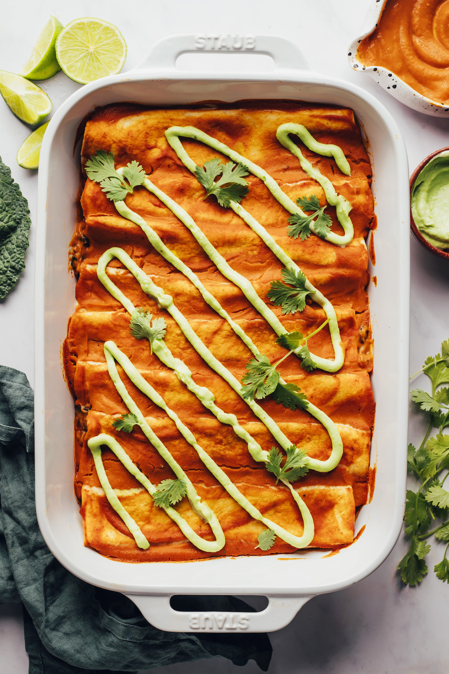 White ceramic baking dish filled with pumpkin black bean enchiladas and topped with avocado crema