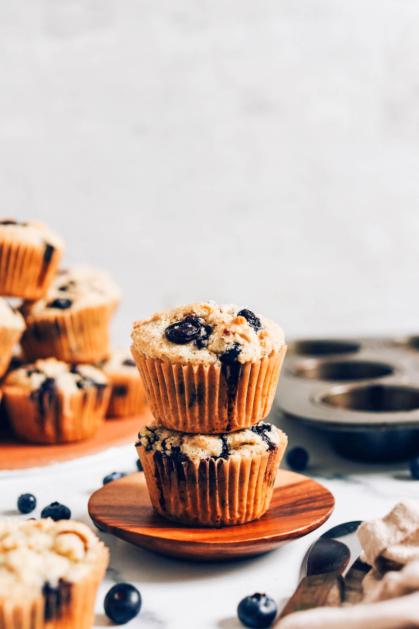 Two vegan gluten-free blueberry muffins on a plate with more muffins in the background and foreground