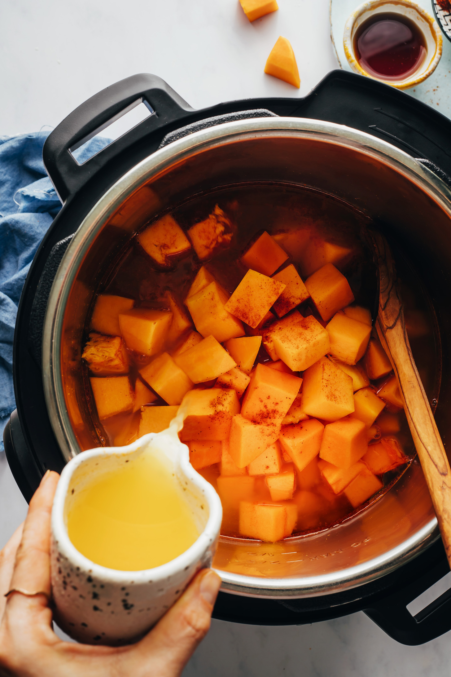 Pouring vegetable broth over cubed butternut squash in the Instant Pot