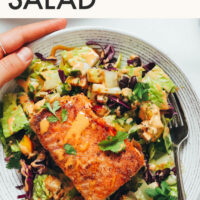 Hands holding a bowl with text above it saying Smoky Summer Salad with Lime-Crusted Salmon