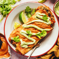 Two pumpkin black bean enchiladas on a plate drizzled with avocado crema
