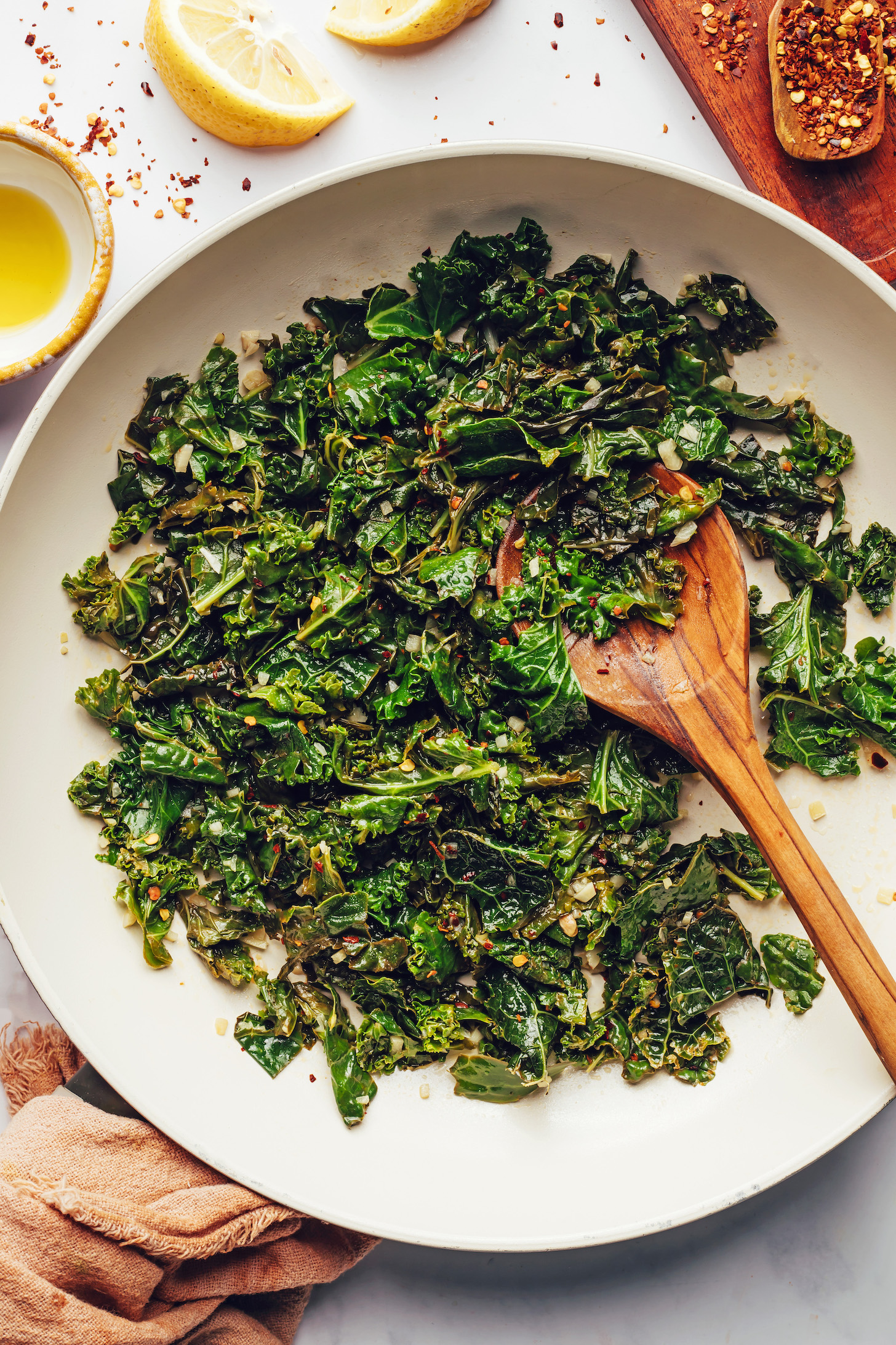 Red pepper flakes, lemon wedges, and olive oil around a pan of sautéed kale