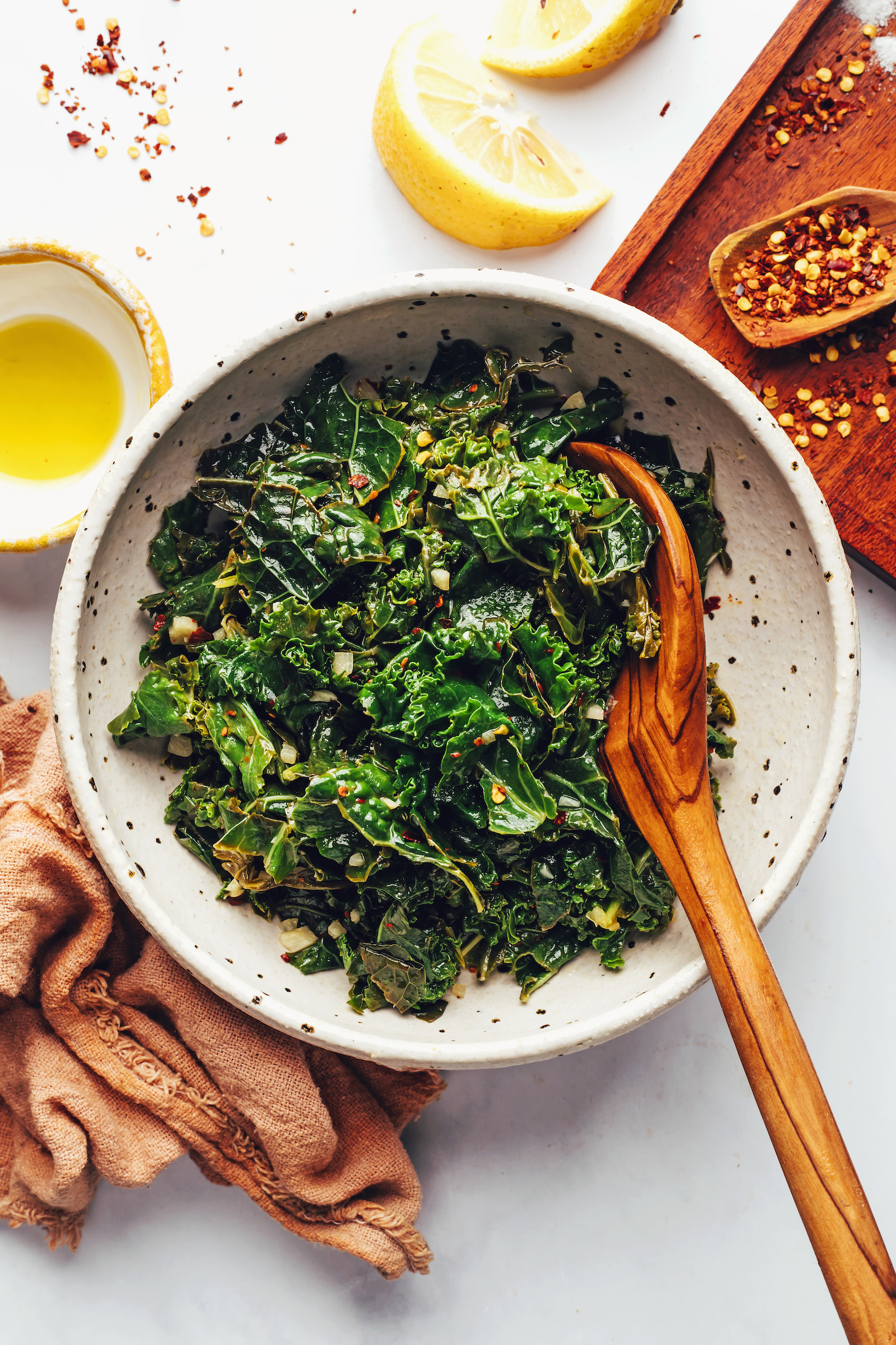 Olive oil, lemon wedges, and red pepper flakes around a bowl of sautéed garlicky greens