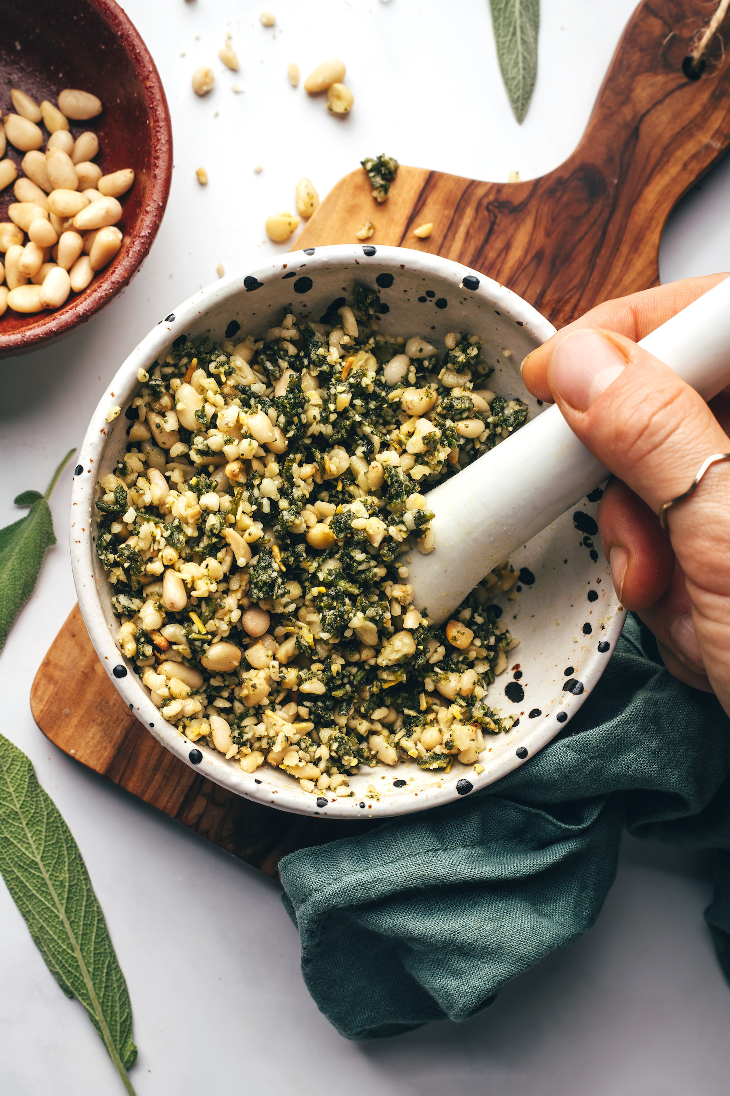 Crushing a pine nut and sage gremolata in a mortar and pestle