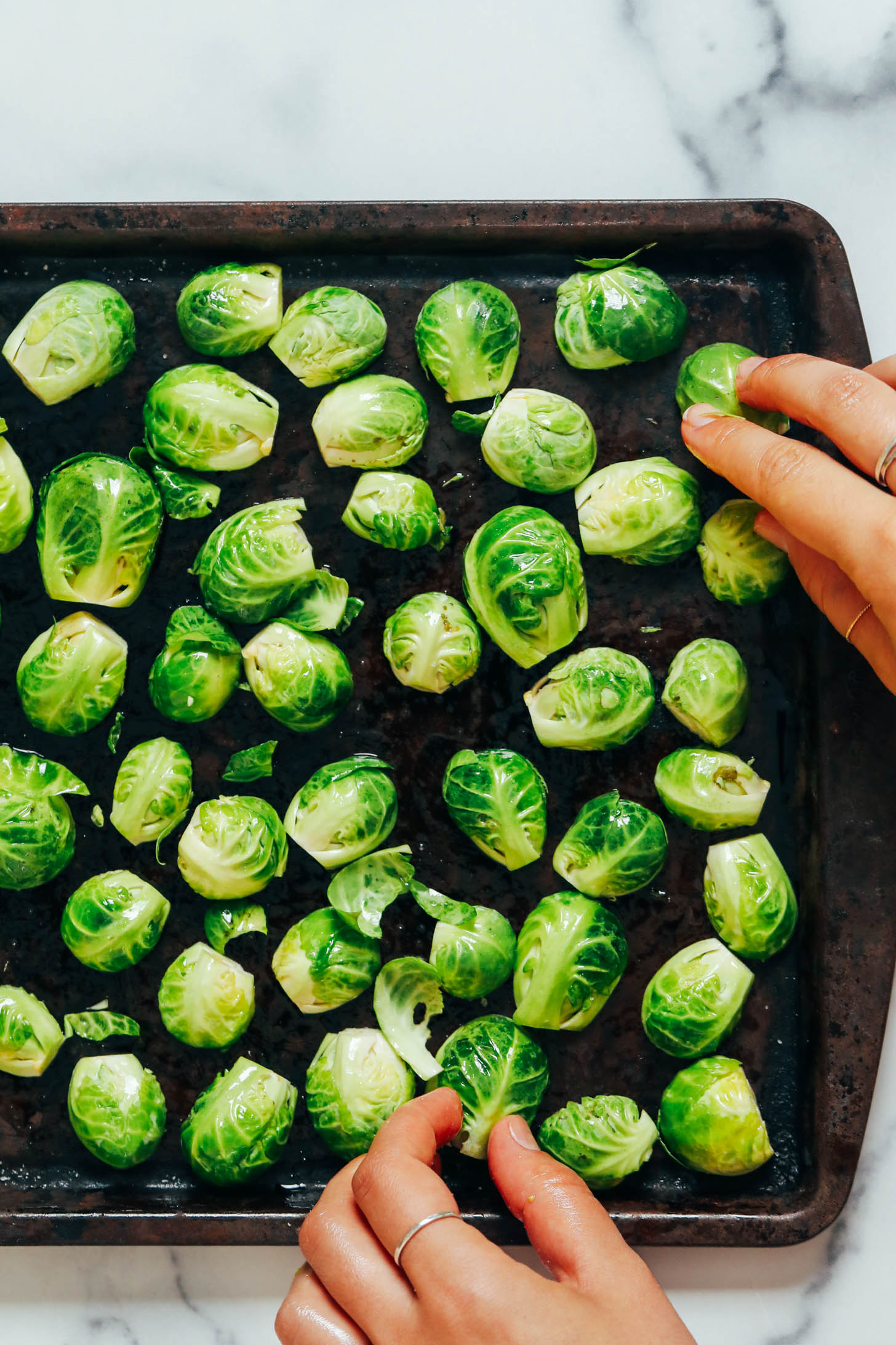 Hands turning Brussels sprouts cut side down on a baking sheet